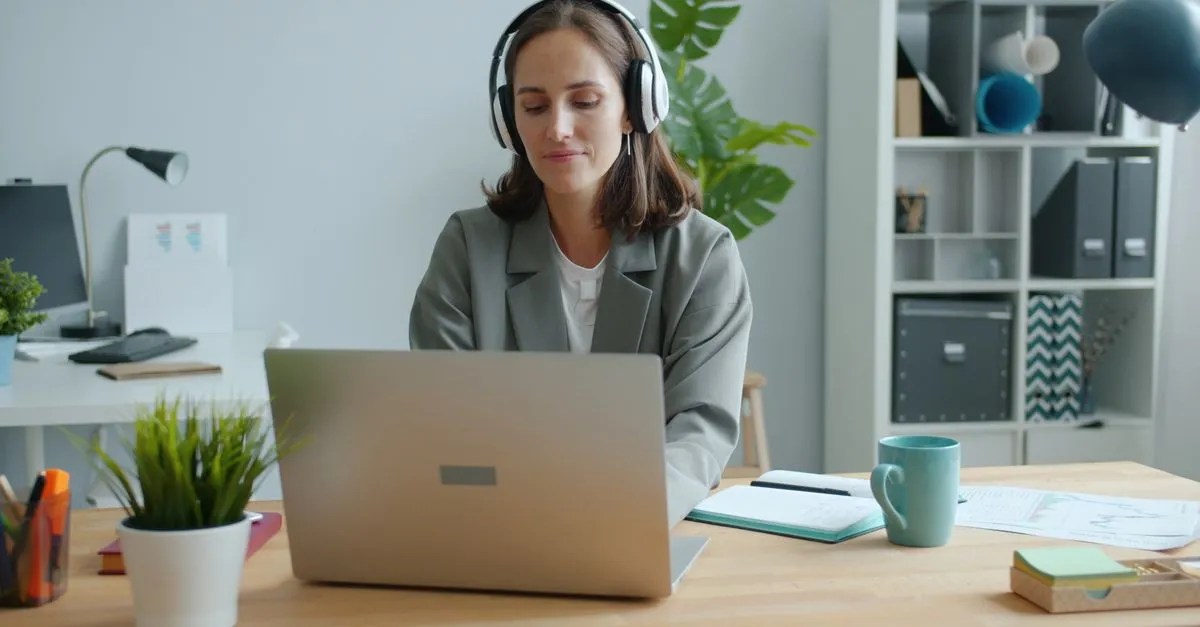 Professional wearing headphones at a computer, automatically turning online meeting video into text.