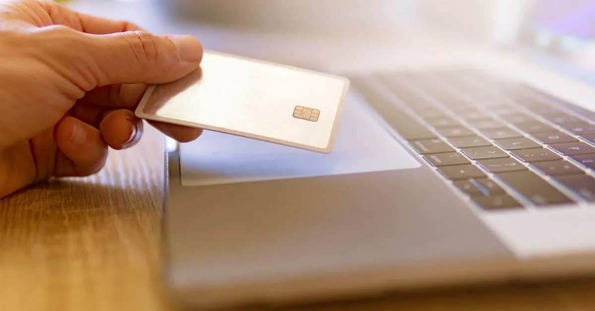 Mão segura cartão crédito sobre laptop, simbolizando gestão financeira para financiamento de imóvel comercial.