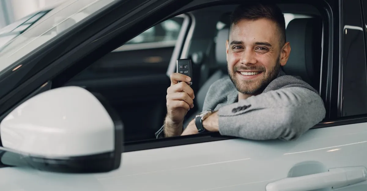 Homem feliz segura chaves ao fechar financiamento de carro usado de forma inteligente.